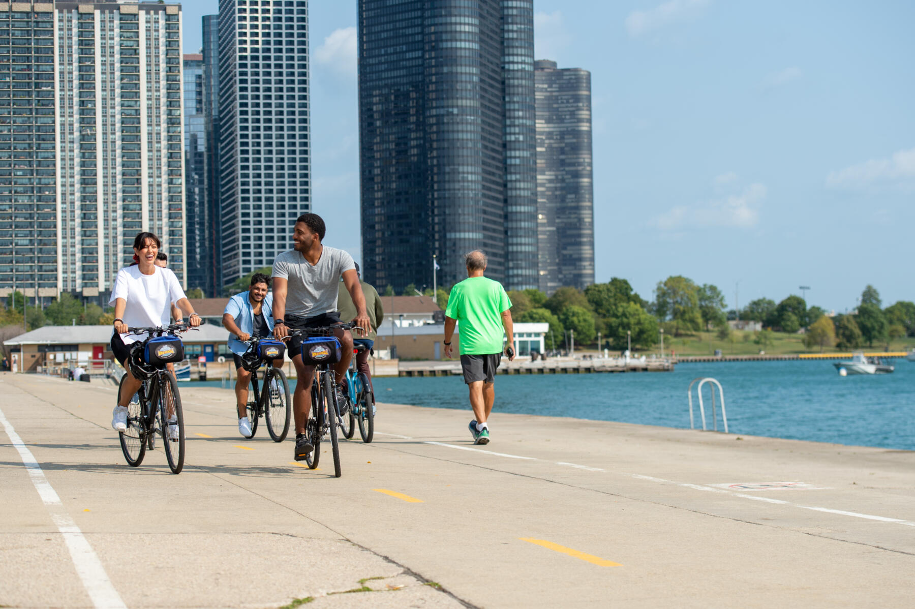 A group of Chicagoans bike on the Lakefront trail with large buildings in the background.