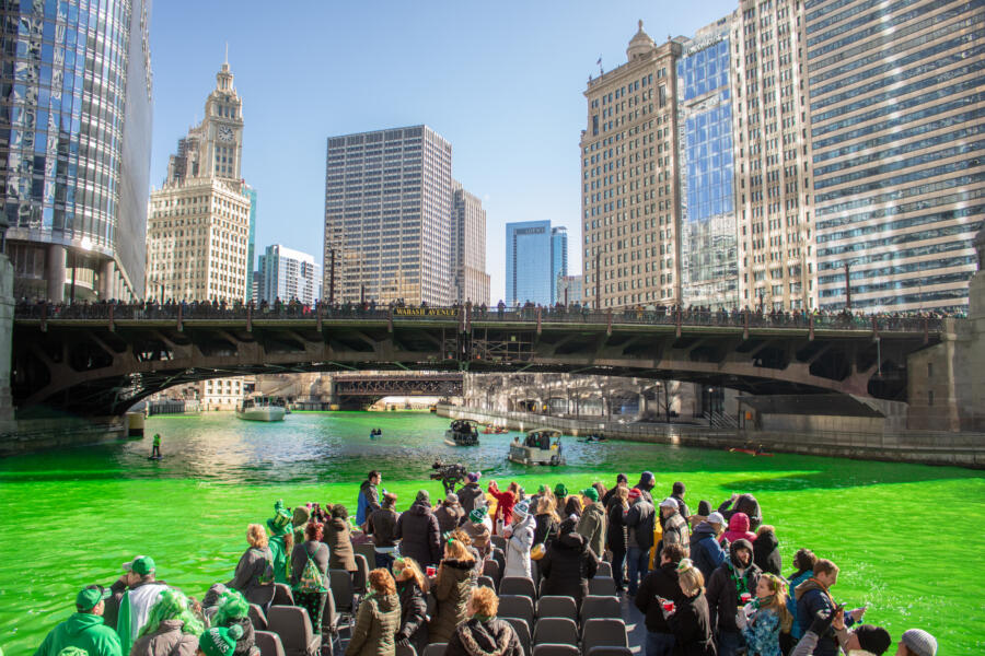 The Seadog boat cruises across the dyed green Chicago river, passing under a big bridge.